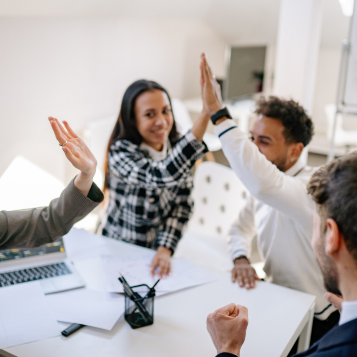 A group of diverse colleagues are celebrating a successful outcome, raising their hands in a high-five gesture.

The scene is composed around a white table, with several people seated around it.  The individuals' positions and actions suggest a collaborative meeting or team gathering.  The focus is centered on the collaborative high-five, with arms raised in the air.  The perspective is from slightly above the table, capturing a dynamic interaction among the group.  The framing emphasizes the moment of celebration, positioning the participants in a close-knit arrangement. Elements are positioned around the high-five action, emphasizing the dynamic nature of the moment.

The key subjects are multiple people of various ethnicities.  They are dressed in casual business attire, displaying expressions of joy and excitement.  The individuals appear to be engaged in a shared moment of triumph, high-fiving and expressing pride and cooperation. 


The artistic medium is photography, likely taken with a smartphone or a camera. The technical execution is sharp and well-lit, capturing the details of the scene.  The style is candid and naturalistic, focused on the group interaction.  No creative choices that go beyond the natural capture of the celebration are evident.

The setting is an office or a similar indoor workspace. The lighting is bright and even, casting no significant shadows, suggesting an office space with overhead lights.  The atmosphere is one of success and accomplishment, with the collaborative action creating a joyful and positive mood.
