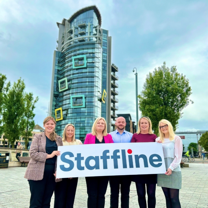 Staffline Recruitment Ireland team standing outside their Belfast headquarters holding a Staffline-branded sign to mark the launch of their recruitment partnership with the Agri-Food and Biosciences Institute (AFBI).