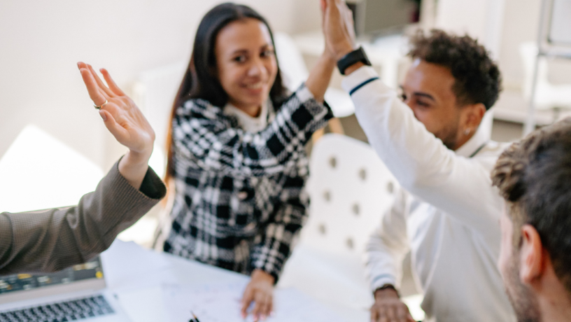 A group of diverse colleagues are celebrating a successful outcome, raising their hands in a high-five gesture.

The scene is composed around a white table, with several people seated around it.  The individuals' positions and actions suggest a collaborative meeting or team gathering.  The focus is centered on the collaborative high-five, with arms raised in the air.  The perspective is from slightly above the table, capturing a dynamic interaction among the group.  The framing emphasizes the moment of celebration, positioning the participants in a close-knit arrangement. Elements are positioned around the high-five action, emphasizing the dynamic nature of the moment.

The key subjects are multiple people of various ethnicities.  They are dressed in casual business attire, displaying expressions of joy and excitement.  The individuals appear to be engaged in a shared moment of triumph, high-fiving and expressing pride and cooperation. 


The artistic medium is photography, likely taken with a smartphone or a camera. The technical execution is sharp and well-lit, capturing the details of the scene.  The style is candid and naturalistic, focused on the group interaction.  No creative choices that go beyond the natural capture of the celebration are evident.

The setting is an office or a similar indoor workspace. The lighting is bright and even, casting no significant shadows, suggesting an office space with overhead lights.  The atmosphere is one of success and accomplishment, with the collaborative action creating a joyful and positive mood.